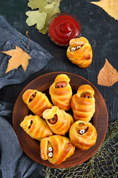 Funny sausage and cutlets mummies in dough with eyes, ketchup on table. Halloween food. Top view. Flat lay