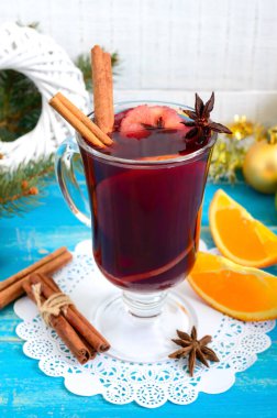 Noel, mavi ahşap bir kırsal masada baharatlı ve meyveli kırmızı şarap. Geleneksel tarçınlı sıcak içecek, kakule, portakal ve anason. Dikey görünüm.