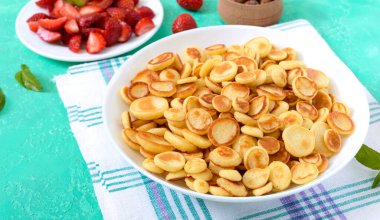 Parlak bir arka planda taze çilek ve fındıklı bir kasede krep gevreği. Lezzetli ve moda bir kahvaltı. Organik Hollanda Mini Krepleri. Gıda eğilimi.