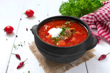 Geleneksel Ukrayna borsch 'u, beyaz ahşap arka planda siyah bir çömlekte taze sebzeler ve et..