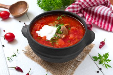 Geleneksel Ukrayna borsch 'u, beyaz ahşap arka planda siyah bir çömlekte taze sebzeler ve et..