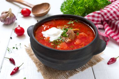 Geleneksel Ukrayna borsch 'u, beyaz ahşap arka planda siyah bir çömlekte taze sebzeler ve et..
