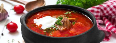 Geleneksel Ukrayna borsch 'u, beyaz ahşap arka planda siyah bir çömlekte taze sebzeler ve et. Pankart