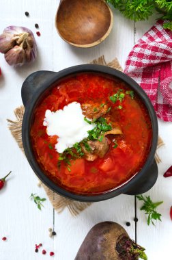 Geleneksel Ukrayna borsch 'u, beyaz ahşap arka planda siyah bir çömlekte taze sebzeler ve et. Üst görünüm.