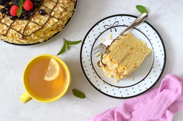 经典的拿破仑蛋糕美味的节日层次分明的甜点 配上油腻的糕点和装饰有新鲜浆果的奶油奶油 还有一杯柠檬茶 — 图库照片