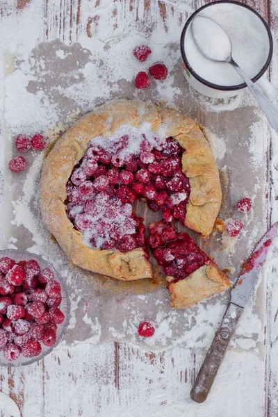 Homemade fruit pie (galette) made with fresh raspberries with powdered sugar on wooden table. Open pie, raspberry tart. Summer berry dessert. Flat lay