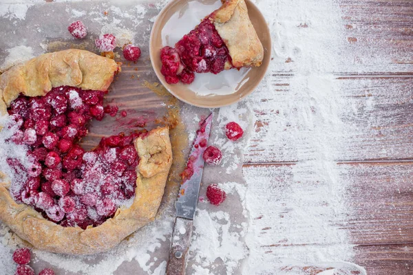 Homemade fruit pie (galette) made with fresh raspberries with powdered sugar on wooden table. Open pie, raspberry tart. Summer berry dessert. Flat lay. Empty space for text, copyspace.