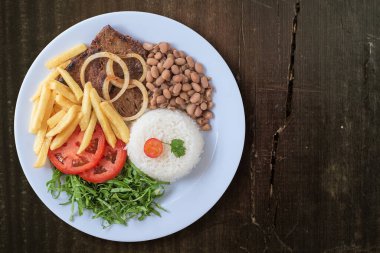 Brezilya yemek tabağı. Fasulye, pilav, et, cips, lahana, domates, soğan. Yönetici yemeği. Bulaşık bitti. Üst Manzara. Ahşap arka planda izole edilmiş