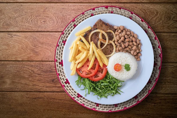 Brazilian food dish. Beans, rice, meat, chips, cabbage, tomatoes, onions. Executive dish. Dish done. Top view. Isolated on wooden background