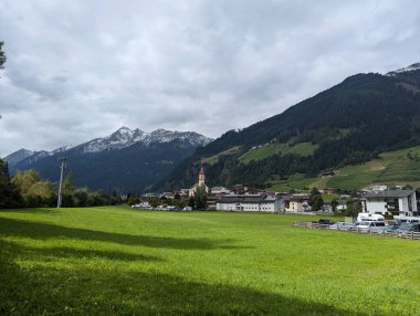 Yeşil çayırlar, sık ormanlar ve kar kaplı dağlarla çevrili bir Avusturya dağlık köyü, kırmızı çatılı çan kulesine sahip bir kiliseye ev sahipliği yapıyor..