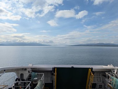 Oban, İskoçya 'dan gelen feribot güvertesi, bulutlu bir gökyüzünün altındaki puslu Mull Adası' na uzanan sakin sulara açılıyor. Sarı korkuluklar ve sakin deniz manzarasını çerçeveleyen yeşil bir rampa..