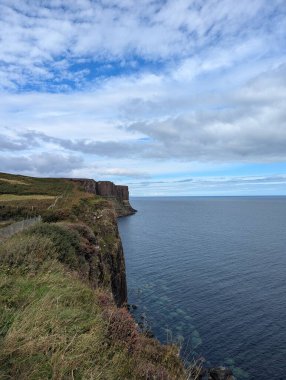 Kilt Kayası 'nın bazalt sütunları Skye Adası' nın kuzeybatı Atlantik sularının üzerinde Jurassic dolerite eşik kulesi tarafından oluşturulmuştur. Bir güvenlik çiti, parçalı bulutlu bir gökyüzünün altındaki uçurumu sarıyor..