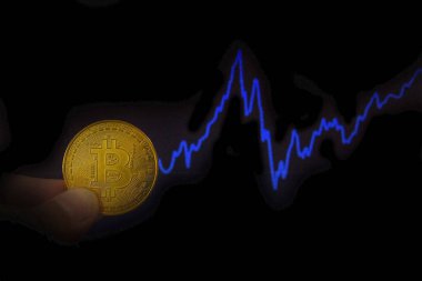 Bir grafik ile karanlık bir arka plan üzerinde bir para bitcoin parmak tutun