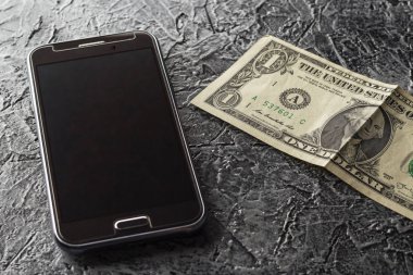 Telefon ve karanlık, türdeş olmayan arka plan üzerinde bir dolar. Siyah, kahverengi, gri, renkli.
