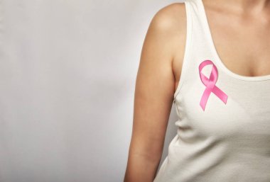 Göğsünde pembe kurdele olan beyaz tişörtlü bir kız..