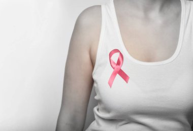 Göğsünde pembe kurdele olan beyaz tişörtlü bir kız..