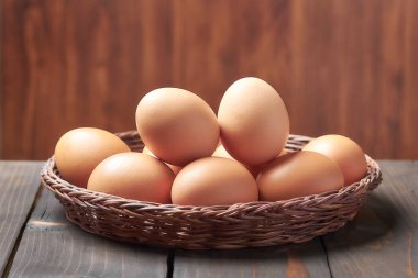 Hasır bir sepetteki tavuk yumurtaları, arka planda bulanıklık olan eski bir ahşap masada..