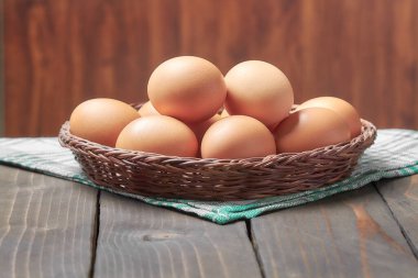 Tahta hasır sepetteki tavuk yumurtaları eski, siyah bir masada.