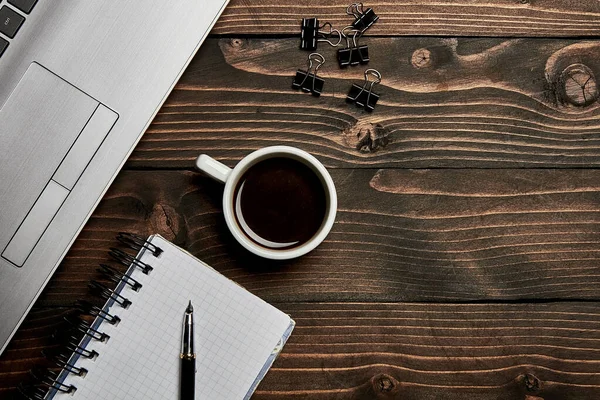 Laptop cup with coffee notebook pen on wooden with roofing. Working table view from the top.