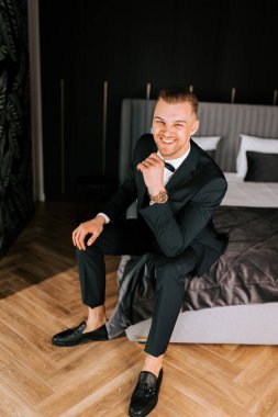 Young man in formal suit sitting on bed in elegantly styled hotel room