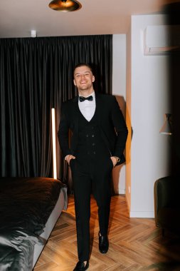 Stylish man in formal attire walking in a modern hotel room during a special event