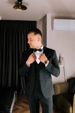 Man adjusts tuxedo in stylish hotel room ahead of formal event