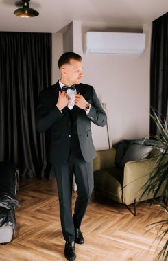 Groom getting ready in elegant suit and bow tie in modern indoor space