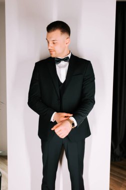 Man in elegant suit adjusting his watch in a stylish indoor setting during evening event
