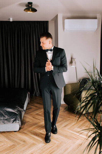 Man in formal attire prepares for event in stylish indoor setting at evening