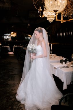 Bride in elegant wedding dress holding bouquet in a beautifully decorated dining venue