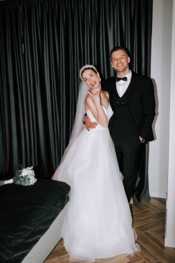 Couple poses joyfully in elegant wedding attire inside a stylish indoor venue