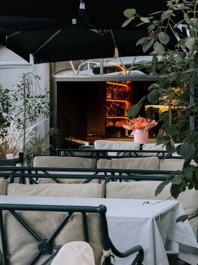 Zarif masaları ve modern bir restoranda şık bir barı olan bir açık hava yemek salonu.