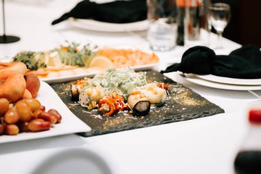 İyi ışıklandırılmış bir mekanda sofistike bir yemek etkinliğinde siyah tahtada servis edilen zarif suşi tabağı.