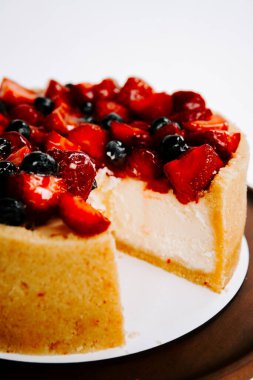 Beyaz arka planda çilek ve yabanmersinli taze yapılmış cheesecake.