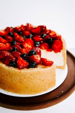 Beyaz arka planda çilek ve yabanmersinli taze meyveli cheesecake.