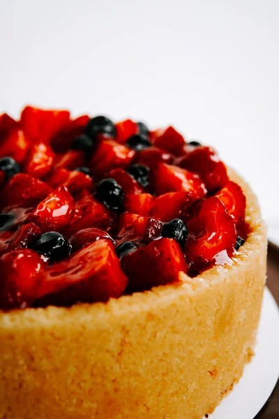 Basit bir arkaplanda meyveli kek sergileniyor.