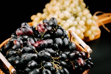 Olgun siyah ve yeşil üzümler sepetin içinde koyu bir zemin üzerinde hasat ve tüketime hazır.