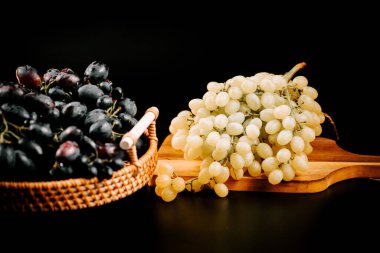 Tahta servis tahtasındaki taze demetlerin yanında duran olgun üzümler.