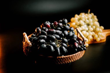 Örülmüş sepetin içinde olgun siyah üzümler ve arka planda altın üzümler.
