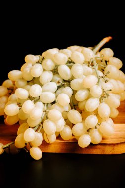 Olgun beyaz üzümler ahşap bir tahtaya dizilmiş, koyu bir arka plana karşı.