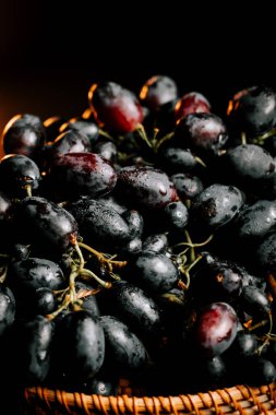 Taze üzümler dokunmuş sepetin içinde yumuşak ışıklandırmalı koyu bir arka planda.