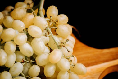 Olgun üzümler ahşap bir yüzeyde dinleniyor canlı renklerini ve dokularını sergiliyorlar.