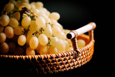 Karanlık bir arka planda dokuma sepetinde olgunlaşmış üzümler.