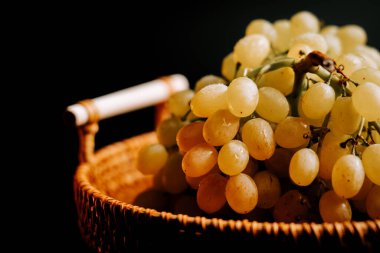 Olgun yeşil üzümler, koyu bir arka planda dokuma sepetinde dizilmiş.