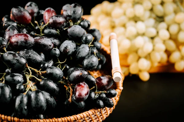 Olgun siyah ve yeşil üzümler, koyu arkaplanda örülmüş sepetler halinde dizilmiş.