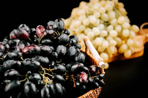 Koyu bir yüzey üzerinde dokuma sepetinde olgun siyah ve yeşil üzümlerin renkli görüntüsü