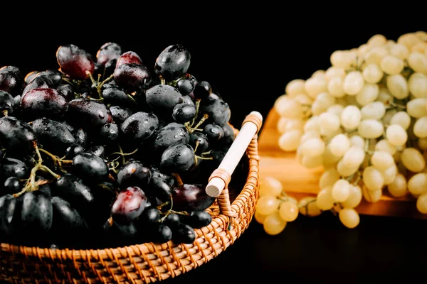 Kırsal ahşap bir yüzey üzerinde yeşil ve siyah çeşitleri sergilenen bir sepette olgun üzümler.