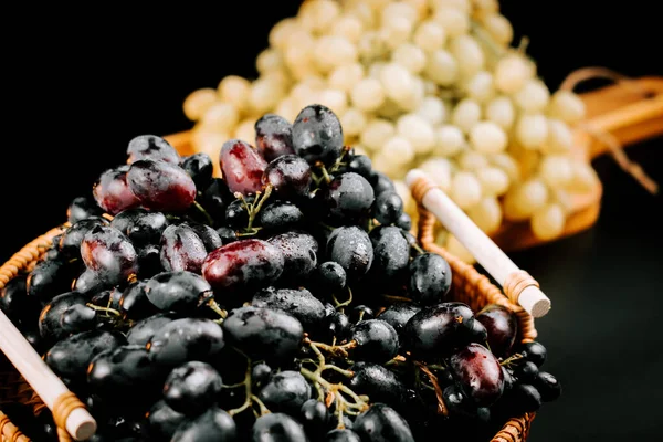 Olgun siyah ve yeşil üzümler sepetin içinde koyu bir zemin üzerinde hasat ve tüketime hazır.