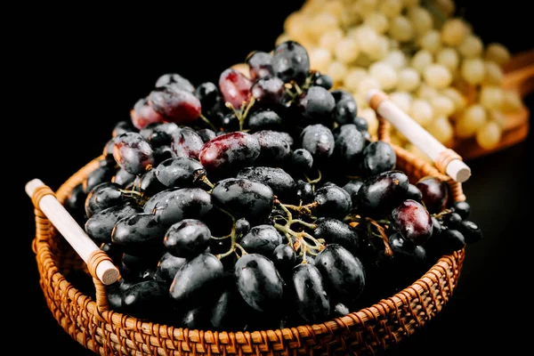 Arka planda taze yeşil üzümlerle dokuma sepetinde sergilenen olgun üzümler.