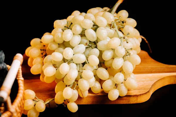 Ahşap kesme tahtasının üzerinde koyu arkaplan ışıklandırmalı olgun üzümler sergileniyor.